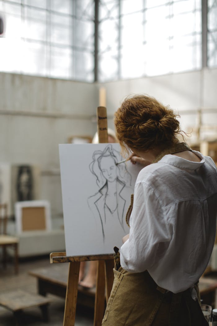 A young woman focuses intently as she sketches on an easel in an art studio.