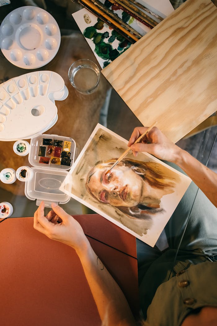 An artist paints a detailed watercolor portrait, surrounded by painting tools and supplies.